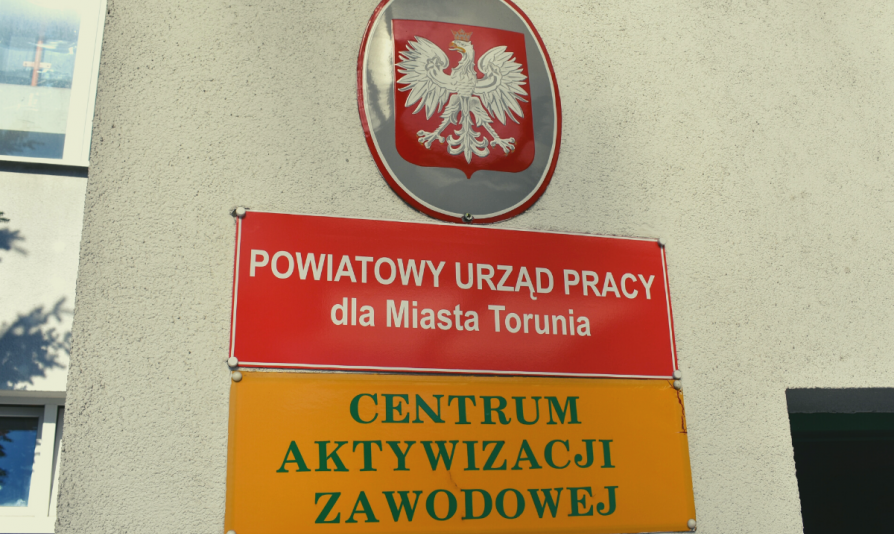Polskie godło i szyldy wiszące przed wejściem do Powiatowego Urzędu Pracy dla Miasta Torunia przy ulicy Mazowieckiej w Toruniu