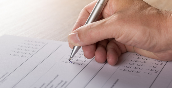 Zdjęcie dłoni trzymającej długopis i wypełniającej ankietę